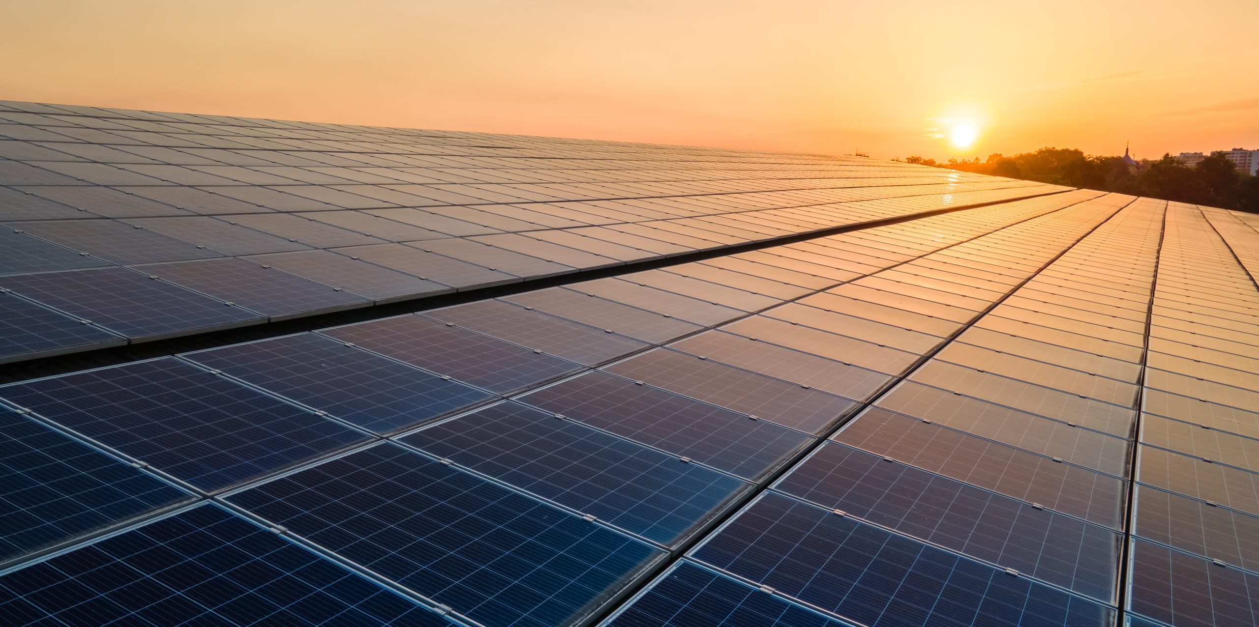 Blue photovoltaic solar panels mounted on building roof for producing clean ecological electricity at sunset. Production of renewable energy concept.